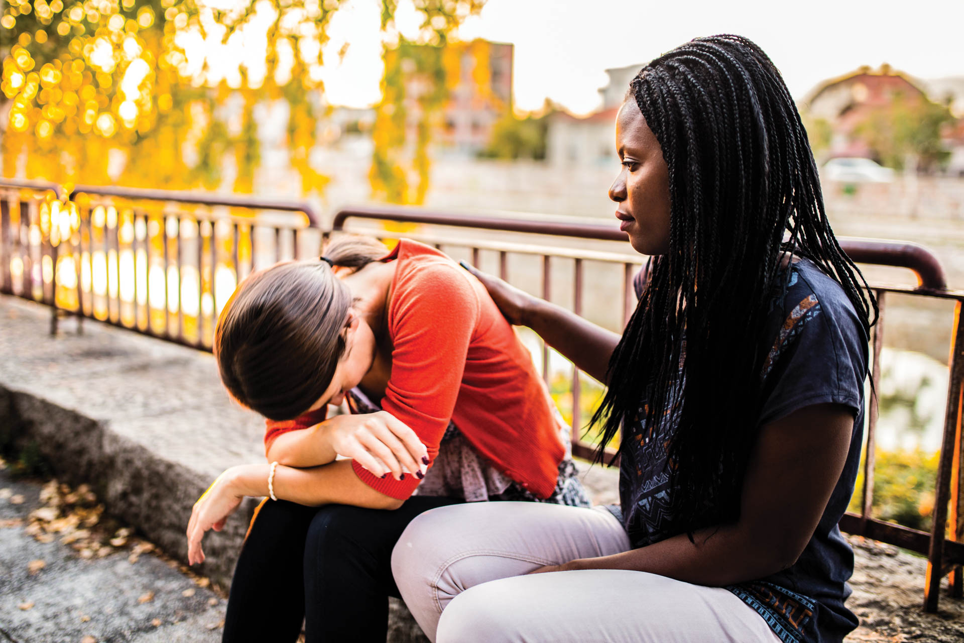 Woman consoling another woman on a bench outside.