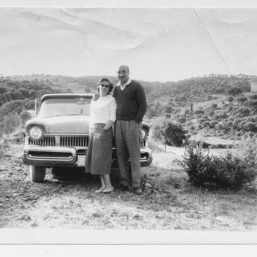 A couple standing in front of their car from the 1950s.