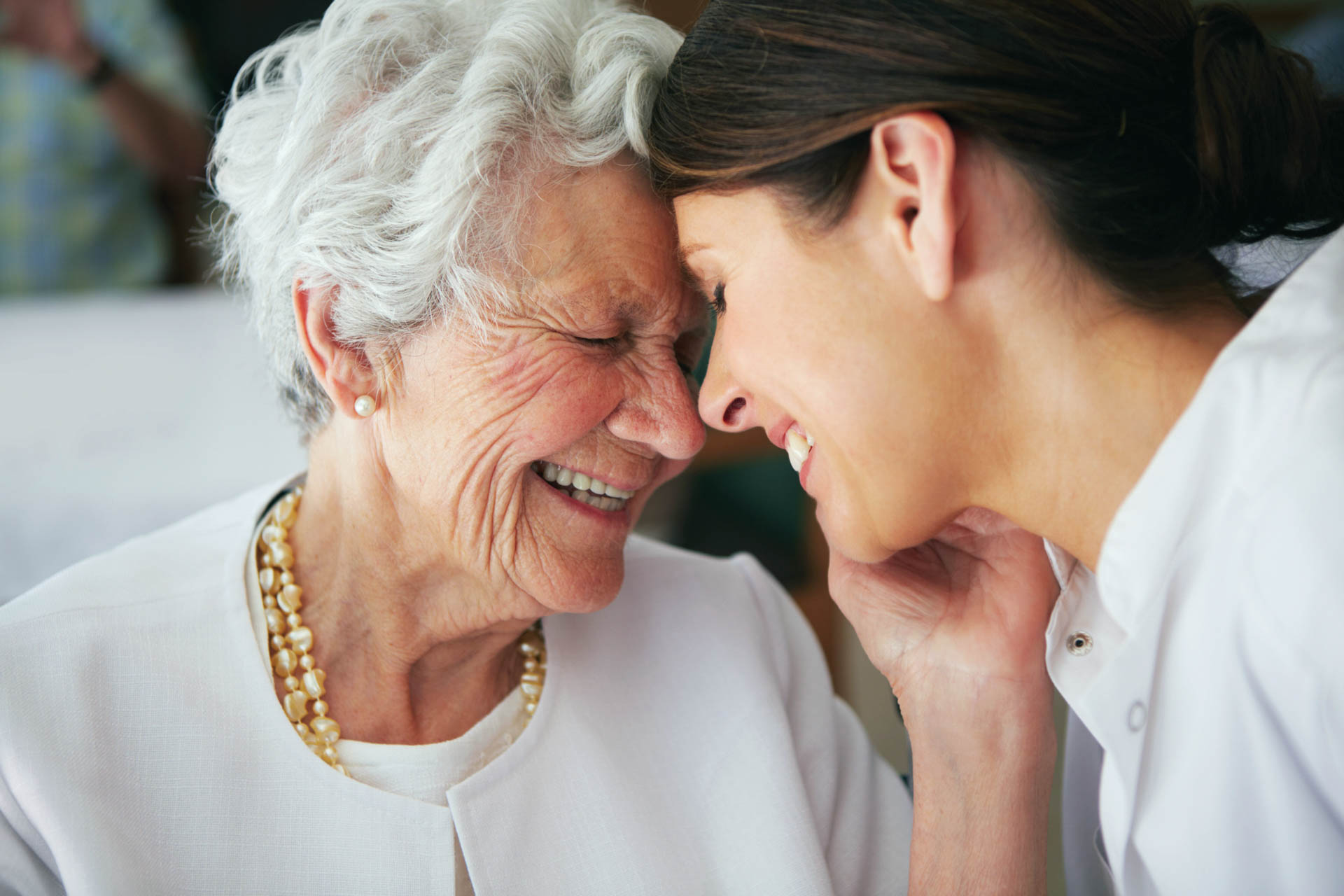 Senior mother and adult daughter smiling with heads together.